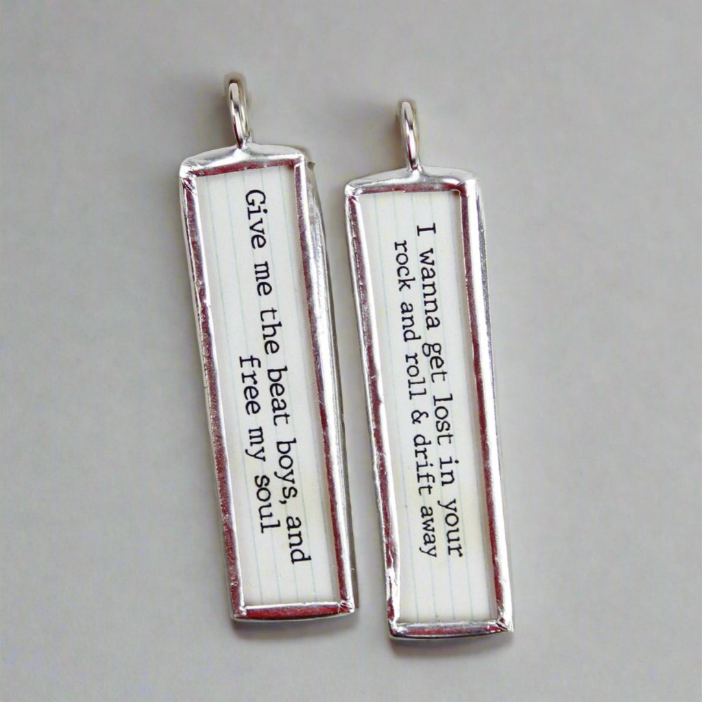 two sided soldered jewelry charms with the lyrics Drift Away on it